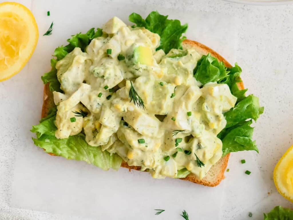 a piece of toast with hardboiled eggs, avocado, and lettuce