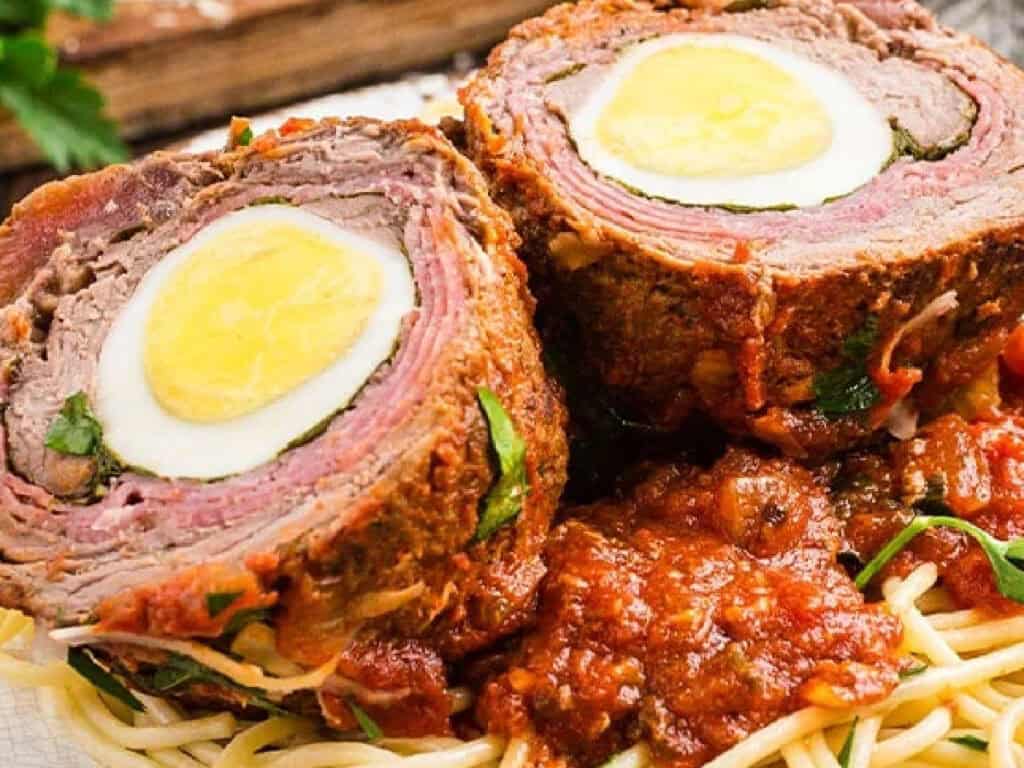 italian braciole that contains hardboiled eggs inside several meats on top of spaghetti with sauce